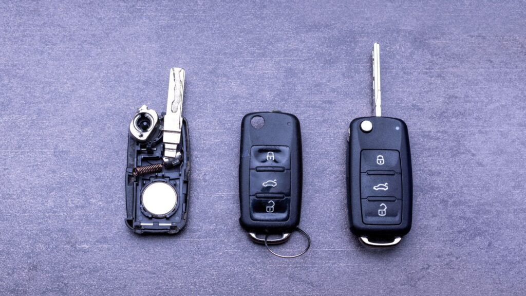 Three car key fobs on a textured surface, one disassembled