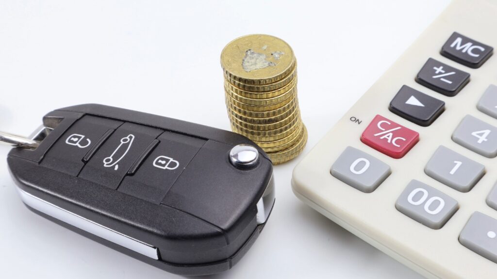 Car key, stack of coins, and calculator on a white background