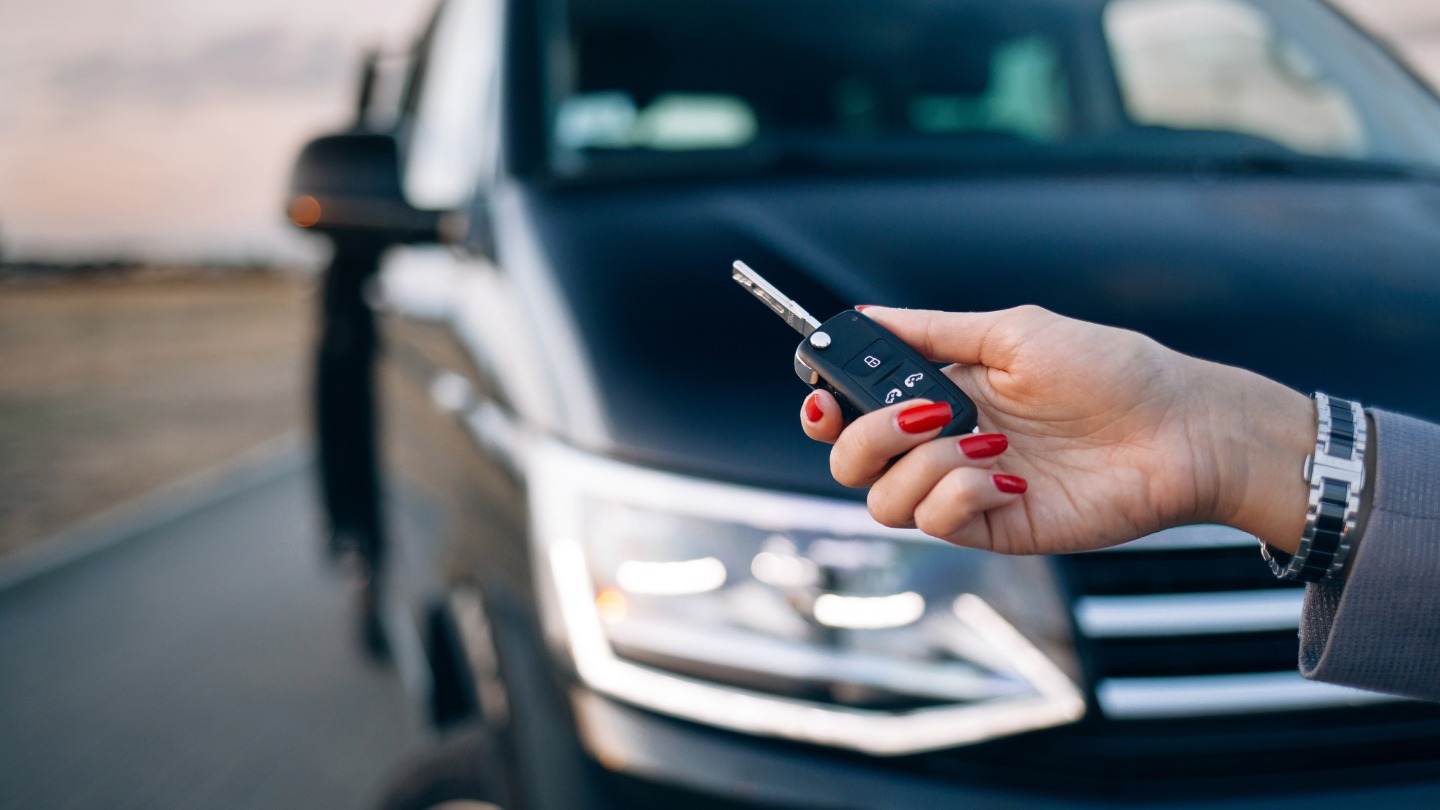 A hand with red nail polish holding a car key in front of a black car
