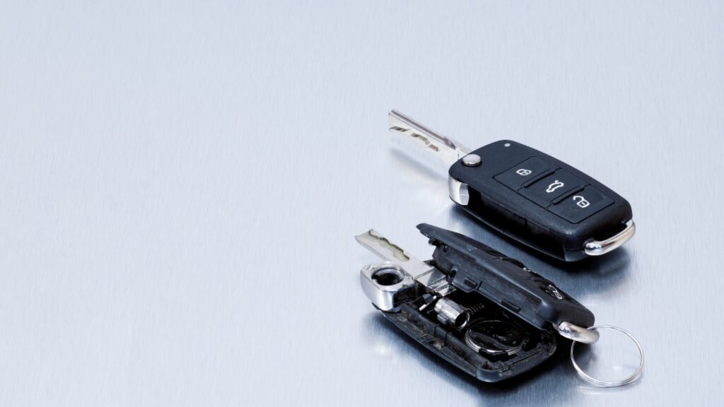 Two car keys on a metallic surface, one with a missing battery